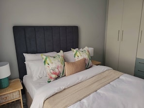 Een bed met witte lakens, een donker hoofdeinde en twee decoratieve kussens.