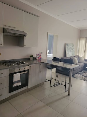 Une cuisine moderne équipée d’une cuisinière à gaz, d’un four et d’une hotte en acier inoxydable. On y trouve un coin repas avec une table et des chaises, ainsi qu’un canapé dans le salon.