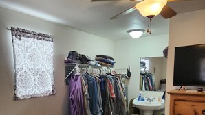 A bedroom with a bed, a dresser, a ceiling fan, a mirror, a TV, and a clothing rack.