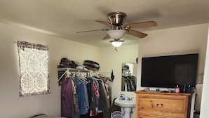 A bedroom with a bed, a ceiling fan, a dresser, a TV, and a closet.