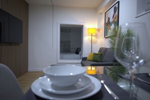 A modern living room with a sofa, a glass coffee table, a dining table with plates, a wine glass, and a lamp. - Newly Refurbished Bradford City Centre Flat (Bradford)