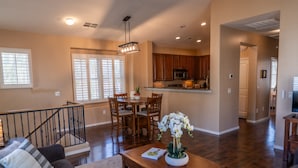 A spacious living area with a dining table, chairs, a coffee table with a plant, a staircase, and a kitchen in the background. - Beautiful 3-bed 2-bath home centrally located in Gilbert with heated pool access (Gilbert)