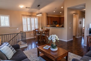 A spacious living area with a dining table, chairs, a coffee table with a plant, a staircase, and a kitchen in the background. - Beautiful 3-bed 2-bath home centrally located in Gilbert with heated pool access (Gilbert)