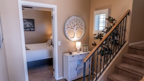 A bedroom with a bed, a nightstand, a wall-mounted tree decoration, a bedside table with a lamp, and a staircase with a railing. - Beautiful 3-bed 2-bath home centrally located in Gilbert with heated pool access (Gilbert)