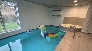 Ein Hallenbad mit einem bunten, aufblasbaren Seehund, einer Whirlpool-Einheit und einem Fenster mit Blick auf Bäume.