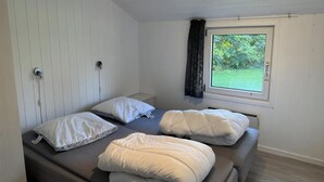 Ein Zimmer mit einem Bett, einem Fenster mit Blick auf Grünflächen und einer Steckdose an der Wand.