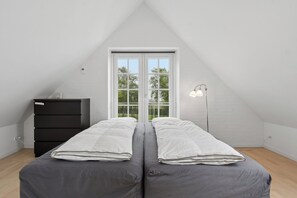 Ein Schlafzimmer mit zwei Betten, einem Schminktisch, einer Lampe und einem Fenster mit Blick auf Bäume.
