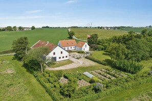 Ein großes, weißes Gebäude mit rotem Dach, umgeben von grünen Feldern und Bäumen.