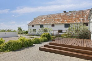 Ein weißes Gebäude mit verrostetem Dach, einer Holzterrasse und einem Kiesweg.