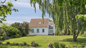 Een huis met een pannendak, omgeven door een verzorgd gazon en een grote boom op de voorgrond.