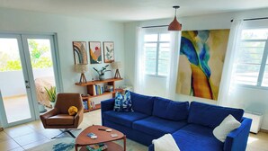 Uma sala de estar com um sofá azul, uma poltrona marrom, uma mesa de centro e uma estante de livros.