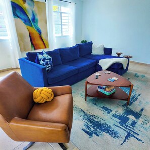 A living room with a blue sofa, a brown leather chair, a wooden coffee table, and a blue patterned rug. - Casa Las Nubes-cayey (Cayey)
