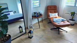 Quarto moderno com cama, poltrona, mesa pequena, espelho e janela.
