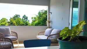 Varanda com mobiliário de vime, uma mesa branca e um vaso com planta.