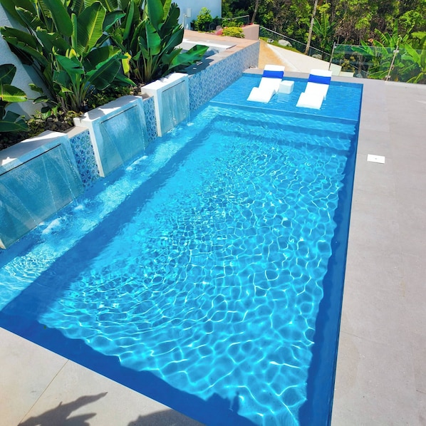 A rectangular swimming pool with clear blue water, surrounded by a tiled deck and a low wall with plants. - Casa Las Nubes-cayey (Cayey)