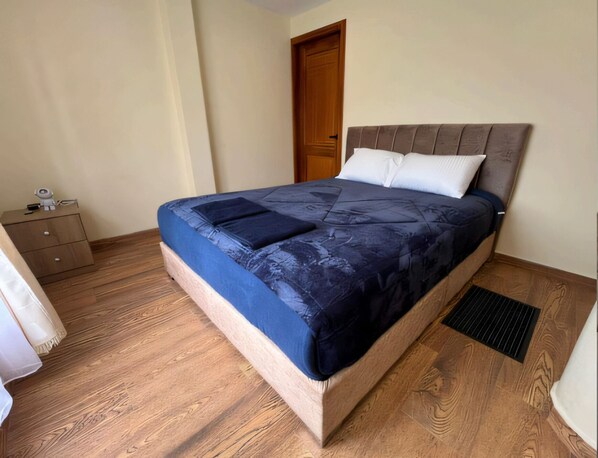 A bedroom with a bed, wooden floor, a nightstand, and a door. - Ecohotel Casa Bola  (Guayllabamba)