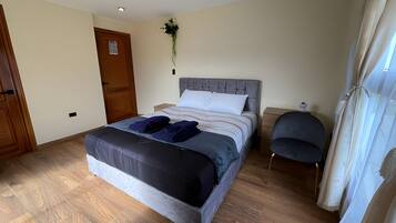 A bedroom with a bed, a chair, a nightstand, a door, and a wall-mounted light fixture.