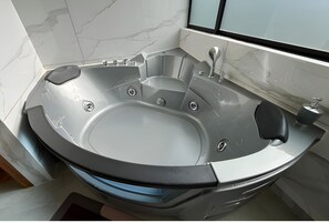 A modern bathroom with a curved bathtub, marble walls, and a window. - Ecohotel Casa Bola  (Guayllabamba)