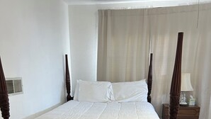 Een hemelbed met een witte quilt, een houten vloer en een nachtkastje met een lamp.