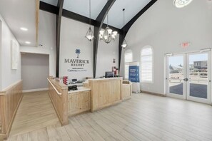 A reception desk with a sign for Maverick Resort, a wooden floor, and a view through the glass doors. - Cozy Studio condo with AC in marvelous Ormond Beach (Ormond Beach)
