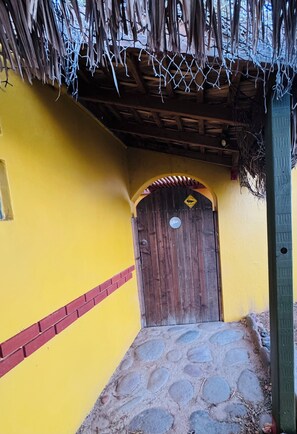 Un bâtiment jaune avec une porte en bois, un chemin de pierre et une toiture en chaume.