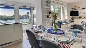 Een eethoek met een tafel gedekt voor vier personen, een keuken op de achtergrond en uitzicht op een brug.