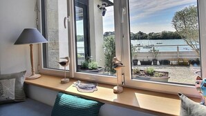 Een kamer met een raamzitje, een lamp, een vogelbeeld en uitzicht op een water met boten.