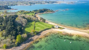 Luchtbeeld van een kustgebied met een strand, helder water en een klein huis in de buurt van de kust.