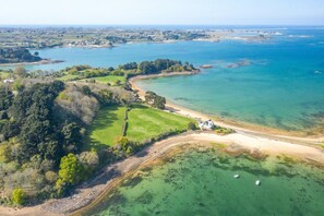Luftaufnahme einer Küstenlandschaft mit Strand, klarem Wasser und einem kleinen Haus in der Nähe des Ufers.