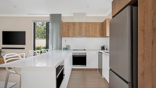Une cuisine moderne avec des meubles blancs, un grand îlot central, un four encastré et un réfrigérateur.