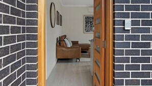 Un couloir avec une porte en bois, des murs en briques noires, un canapé en cuir marron et une œuvre d’art encadrée accrochée au mur.