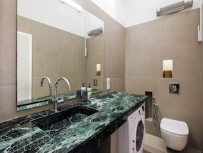 A modern bathroom with a marble sink, a built-in mirror, a toilet, and a washing machine.