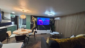 A modern living room with a dining area, a TV mounted on the wall, and a kitchen in the background. - Cozy Private Retreat (Phoenix)