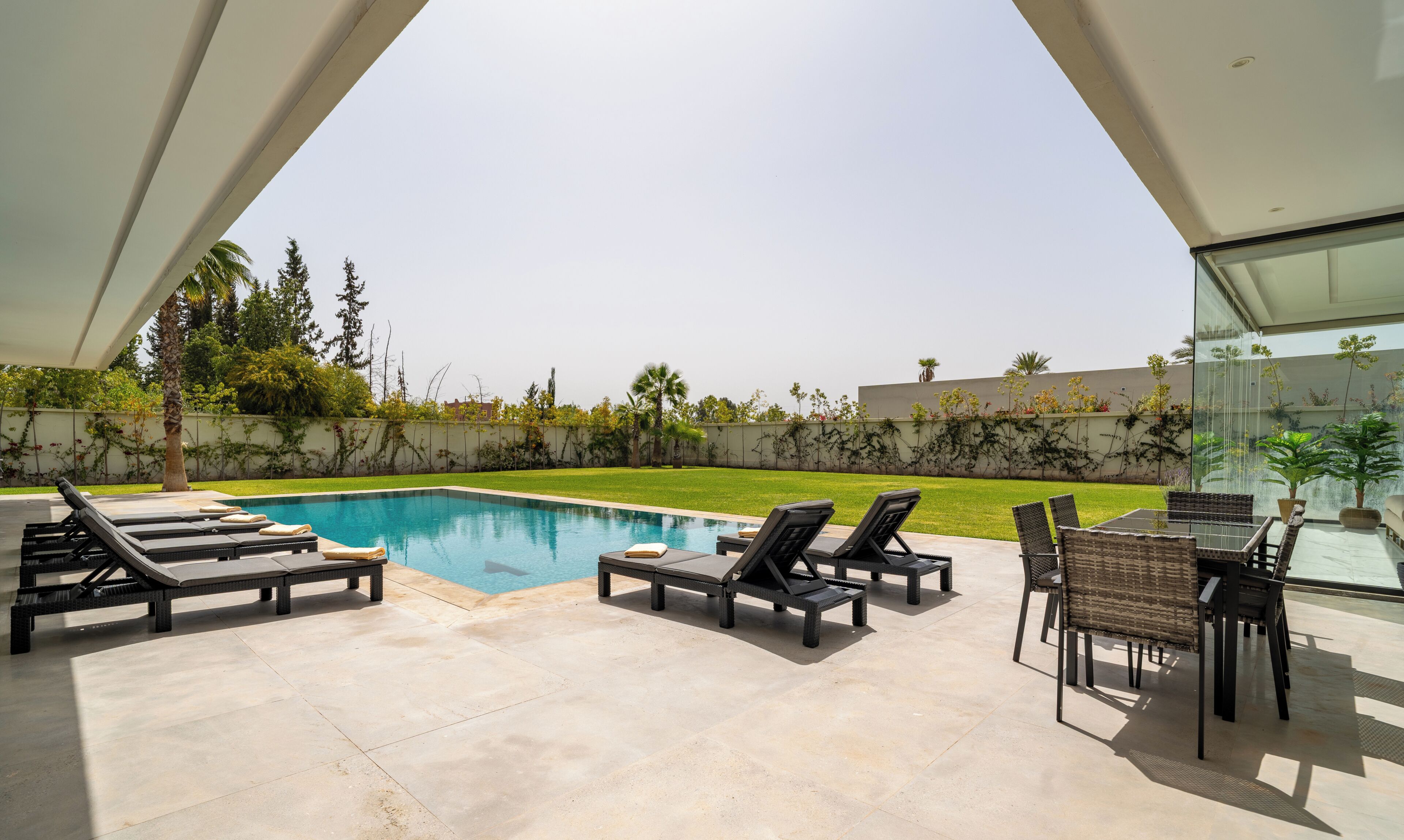 A modern outdoor pool area with lounge chairs and a dining table.
