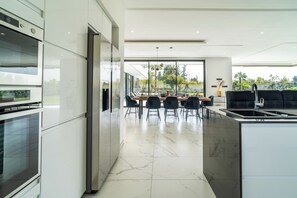 Une cuisine moderne avec un coin repas, de grandes fenêtres et une vue sur l’extérieur.
