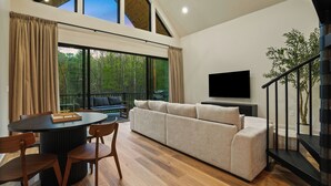A modern living room with a round table, sofa, and TV. - Spiral Loft · Hot Tub · Spa Bath | Lux Sleeps 4 (McArthur)
