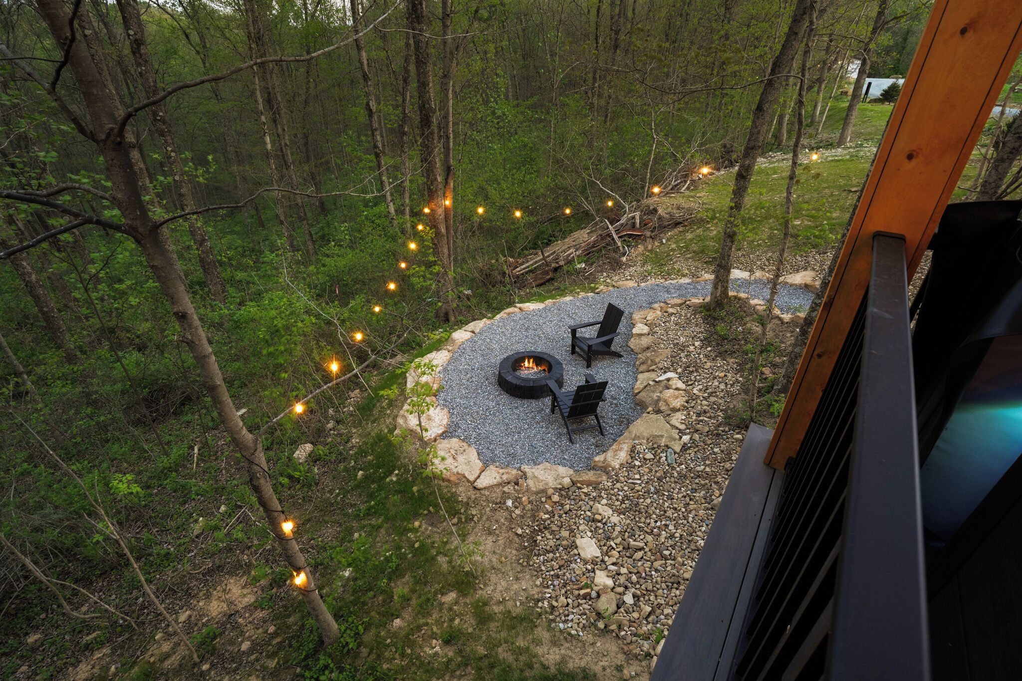 Un espace extérieur circulaire aménagé avec des sièges, doté d’un foyer, et entouré d’un chemin de gravier et d’arbres.
