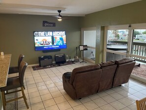 A living room with a television displaying 'The Law Archive,' a couch, a dining table with chairs, and a balcony with a view of the street.