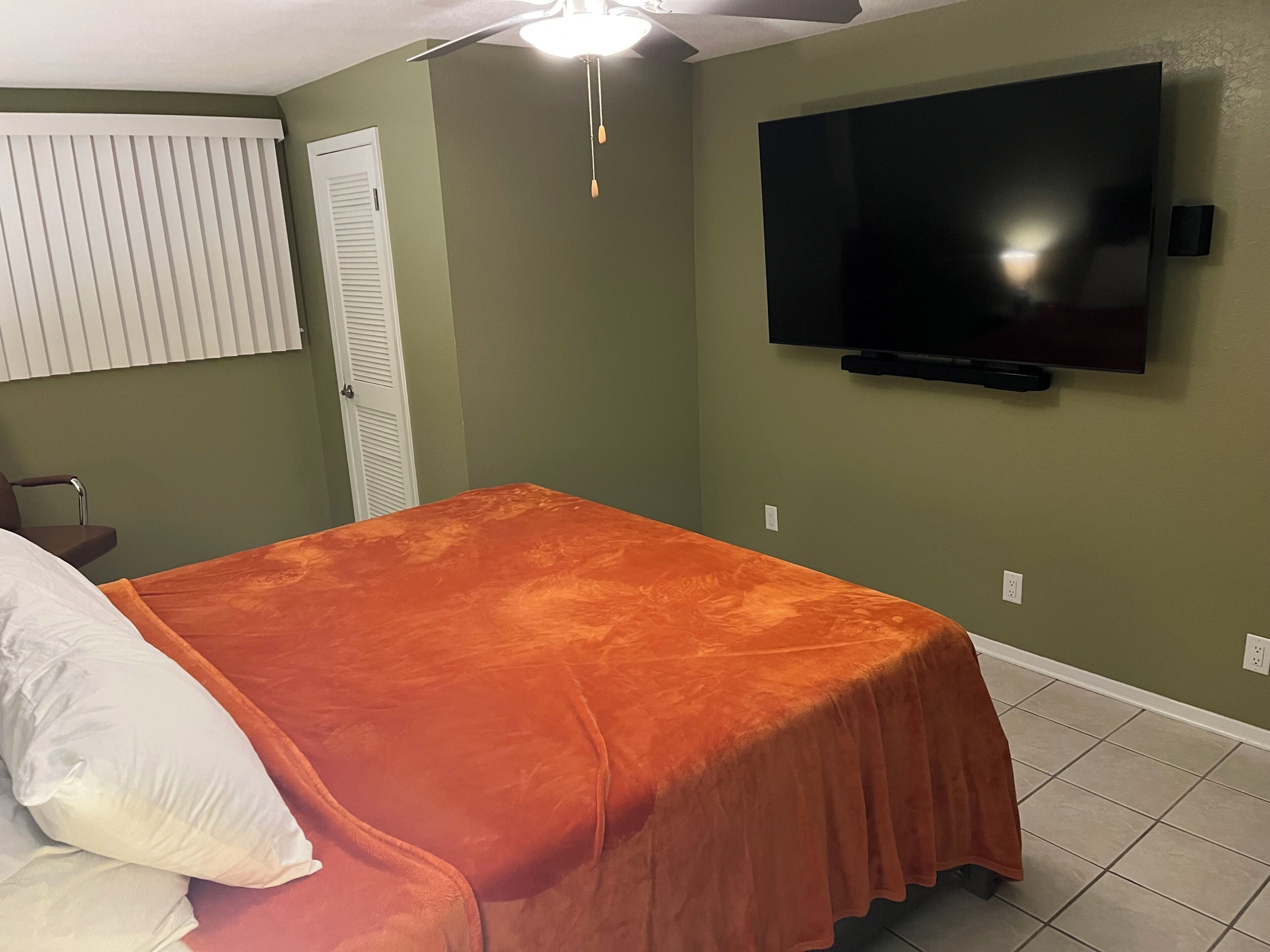 Un dormitorio con cama, ventilador de techo, televisión y puerta.