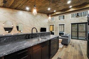 Eine moderne Küche mit Granit-Arbeitsplatte, schwarzen Schränken, einem schwarzen Wasserhahn und einem eingebauten Backofen. Zwei Pendelleuchten, ein großes Fenster und eine Glastür zu einer Terrasse sind vorhanden.
