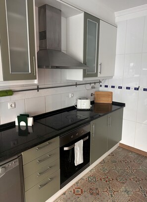 A kitchen with a black countertop, stainless steel appliances, and a patterned floor. - Apartment Santa Maresia [Santa Luzia] (Santa Luzia)