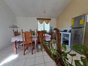 Un coin repas avec une table et des chaises, une cuisine équipée d’un réfrigérateur et une fenêtre avec des rideaux.