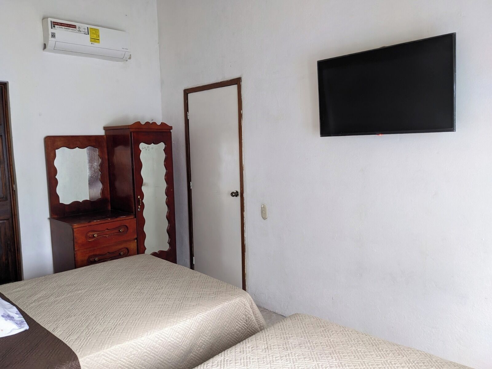Une pièce comprenant un lit, une commode, un téléviseur fixé au mur et une porte.