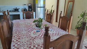 Un comedor con mantel estampado, sillas de madera, refrigerador, estufa y plantas en macetas.