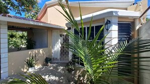 Una casa con porche cubierto, un portón de metal y plantas en macetas.
