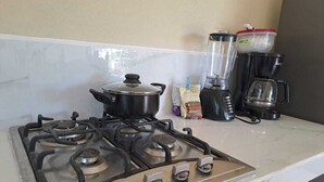 Una cocina con estufa a gas, una olla, una licuadora y una cafetera.
