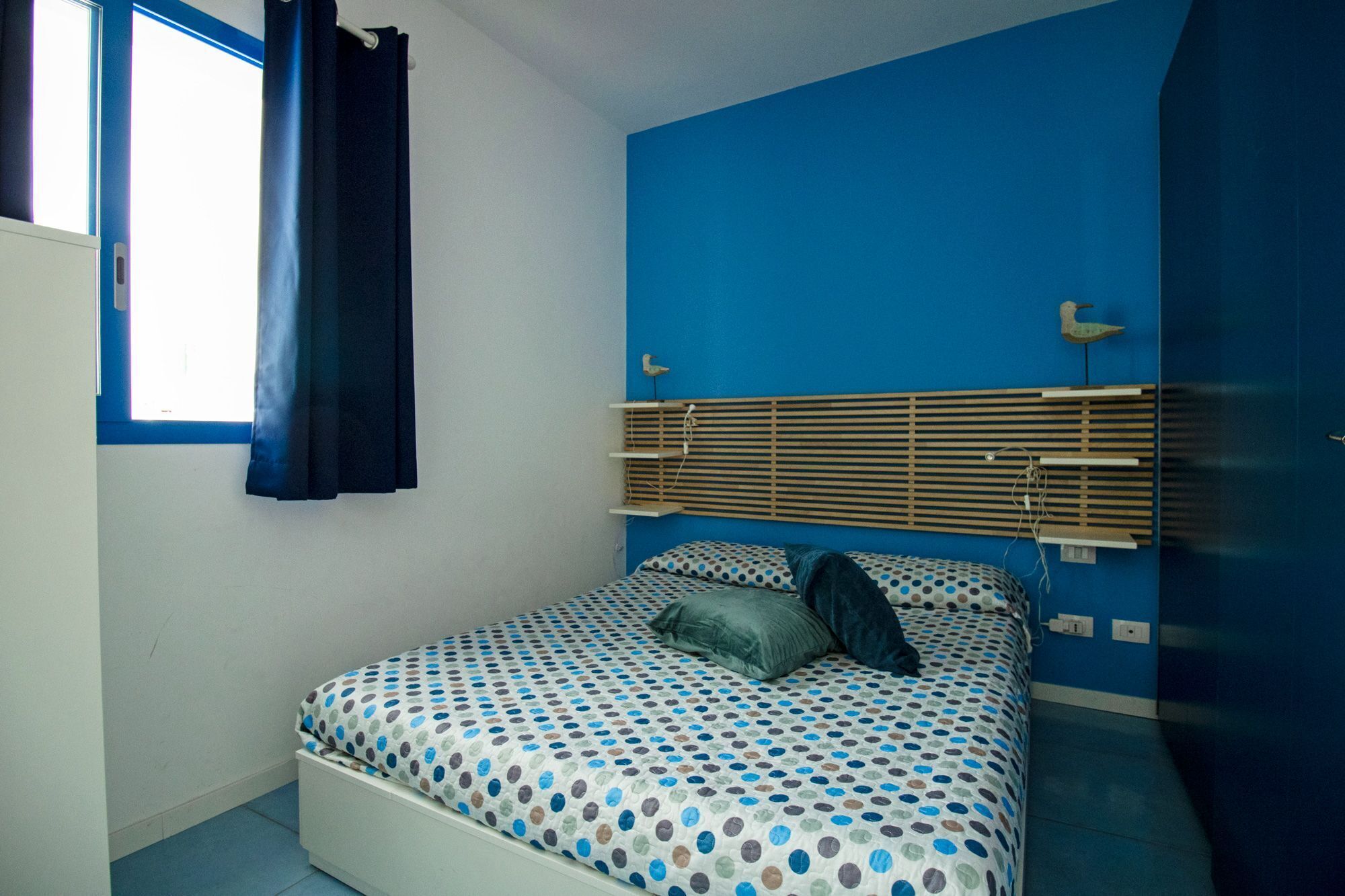 Une chambre à coucher avec un lit, une fenêtre avec des rideaux, un mur bleu et une tête de lit en bois.