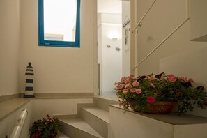 A staircase with a potted plant of pink flowers, a lighthouse decoration, and a window with a blue frame. - Blue House Relax -Cozy family apartment 3 minutes from the sea (Marina di Ragusa)