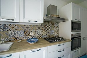 A kitchen with white cabinets, a gas stove, an oven, a microwave, and patterned tile backsplash. - Blue House Relax -Cozy family apartment 3 minutes from the sea (Marina di Ragusa)