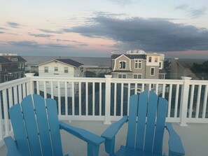 Un balcon avec des fauteuils Adirondack bleus donnant sur une plage, avec des maisons en arrière-plan.
